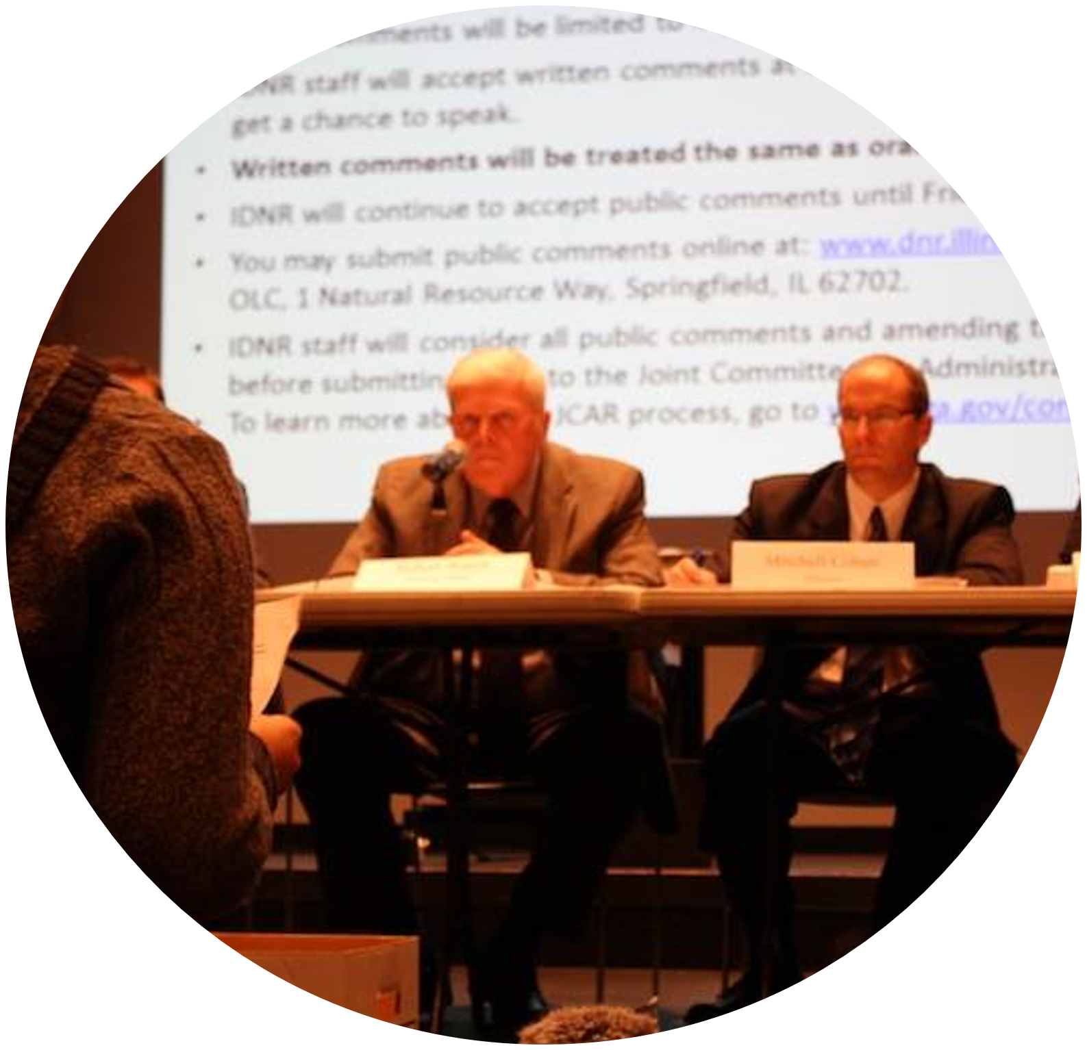 two men sitting at a table in front of a slideshow