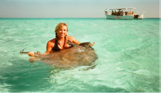 A photograph shows a woman standing in the ocean holding a stingray.